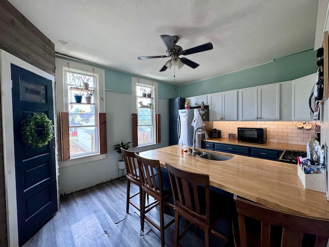 kitchen with butcher block counters, sink, light hardwood / wood-style flooring, stainless steel fridge, and white cabinets