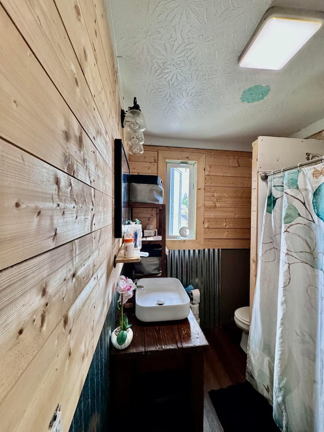 bathroom featuring wooden walls, a textured ceiling, and toilet