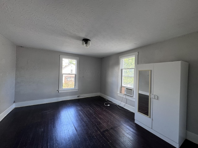 spare room with a textured ceiling, dark hardwood / wood-style flooring, a wealth of natural light, and cooling unit