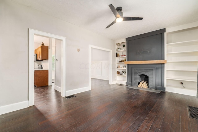 unfurnished living room featuring built in shelves, dark hardwood / wood-style flooring, a textured ceiling, and a brick fireplace