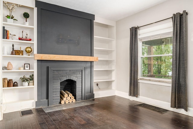 unfurnished living room with built in shelves, dark hardwood / wood-style flooring, a textured ceiling, and a brick fireplace