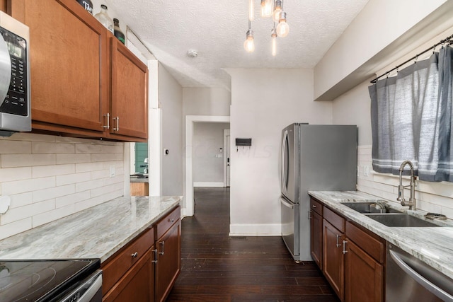 kitchen with appliances with stainless steel finishes, light stone counters, a textured ceiling, dark wood-type flooring, and sink