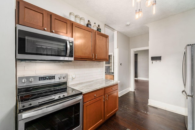 kitchen featuring backsplash, dark wood-type flooring, a textured ceiling, light stone counters, and stainless steel appliances