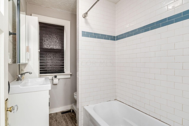 full bathroom featuring wood-type flooring, a textured ceiling, toilet, vanity, and tiled shower / bath