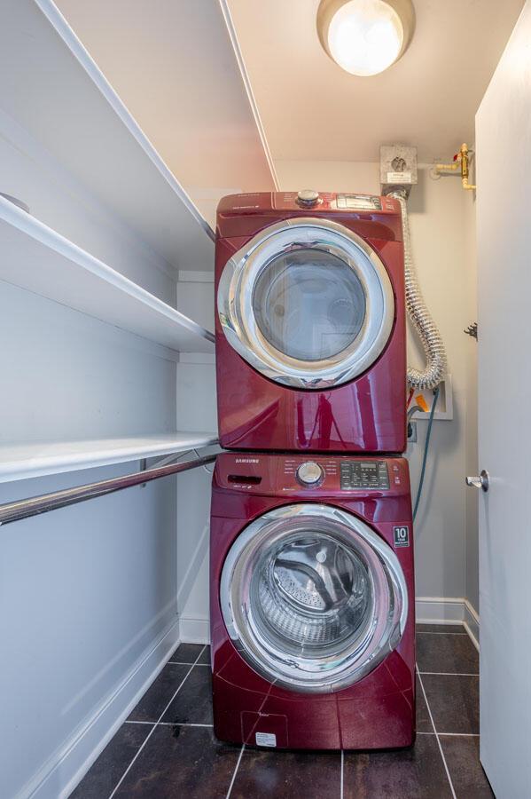 laundry area featuring dark tile patterned flooring and stacked washer / drying machine