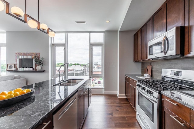 kitchen with appliances with stainless steel finishes, dark hardwood / wood-style flooring, sink, decorative light fixtures, and dark stone countertops