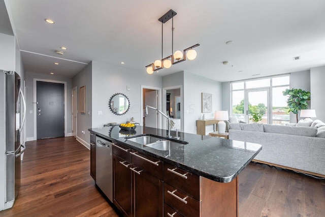 kitchen with a center island with sink, sink, dark hardwood / wood-style floors, dark stone countertops, and stainless steel appliances