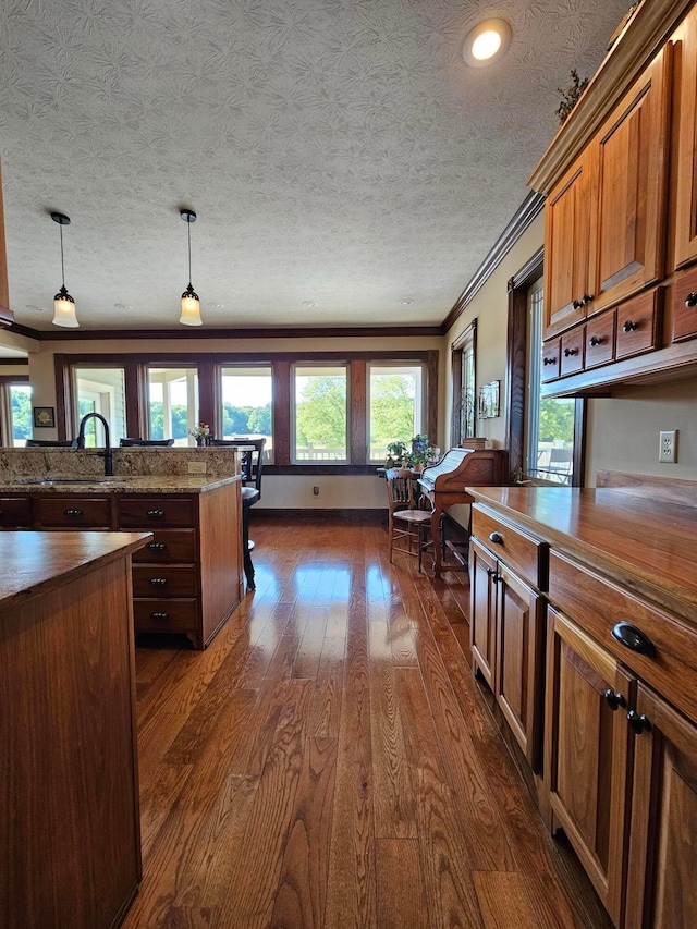 kitchen with dark wood-type flooring, hanging light fixtures, dark stone countertops, ornamental molding, and a textured ceiling