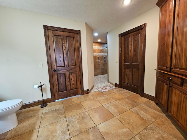 bathroom featuring tile patterned floors, a tile shower, a textured ceiling, and toilet