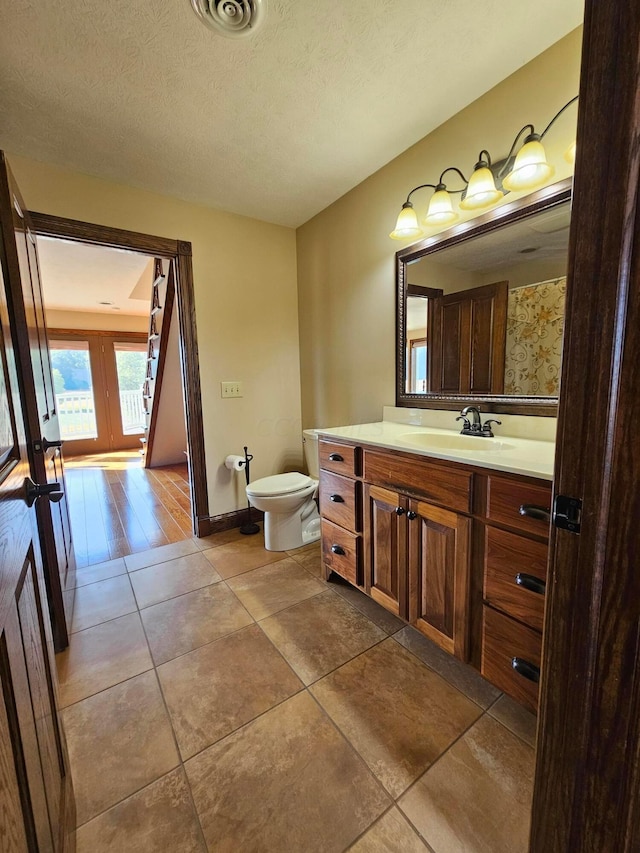 bathroom with french doors, a textured ceiling, toilet, vanity, and hardwood / wood-style flooring