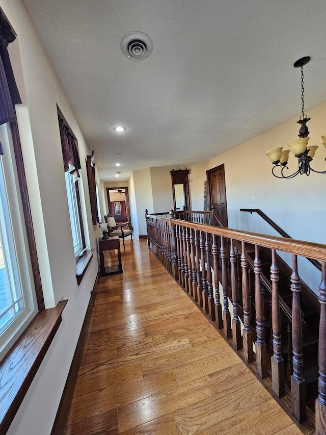 hall featuring hardwood / wood-style flooring, a textured ceiling, and an inviting chandelier