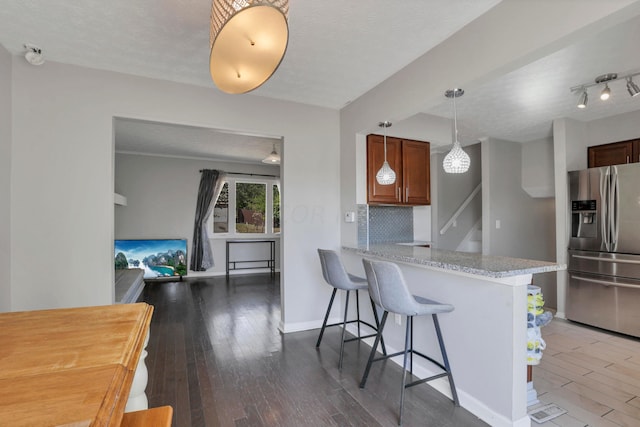 kitchen featuring dark wood-type flooring, stainless steel fridge, a textured ceiling, kitchen peninsula, and a breakfast bar area