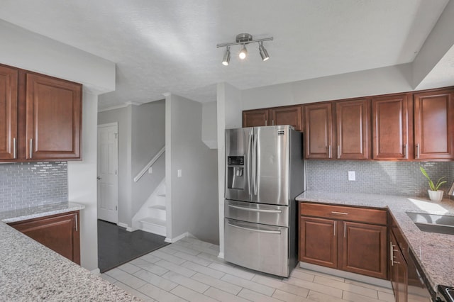 kitchen featuring decorative backsplash, stainless steel refrigerator with ice dispenser, light stone countertops, a textured ceiling, and sink