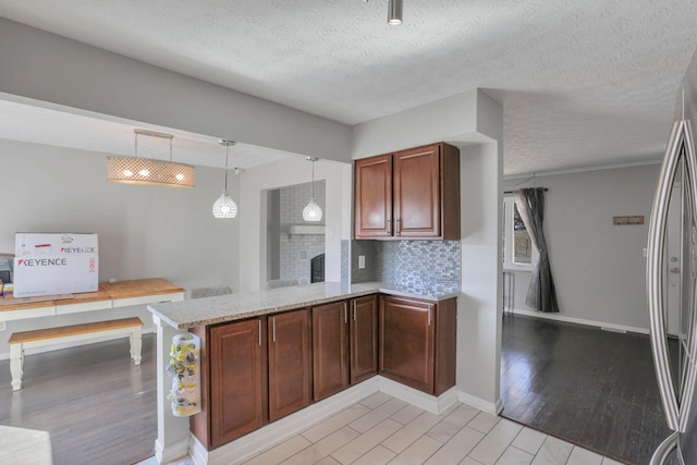 kitchen with kitchen peninsula, stainless steel fridge, light hardwood / wood-style floors, and a textured ceiling