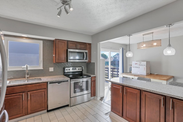 kitchen with light stone countertops, sink, hanging light fixtures, stainless steel appliances, and a textured ceiling