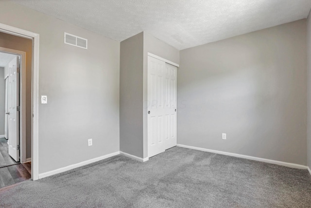 unfurnished bedroom featuring a textured ceiling, dark carpet, and a closet