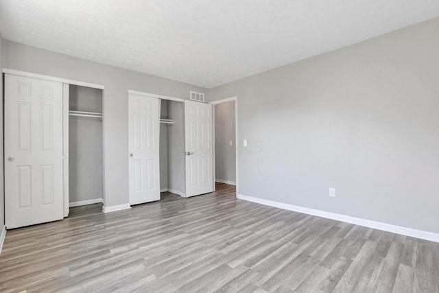 unfurnished bedroom with two closets, a textured ceiling, and light hardwood / wood-style flooring