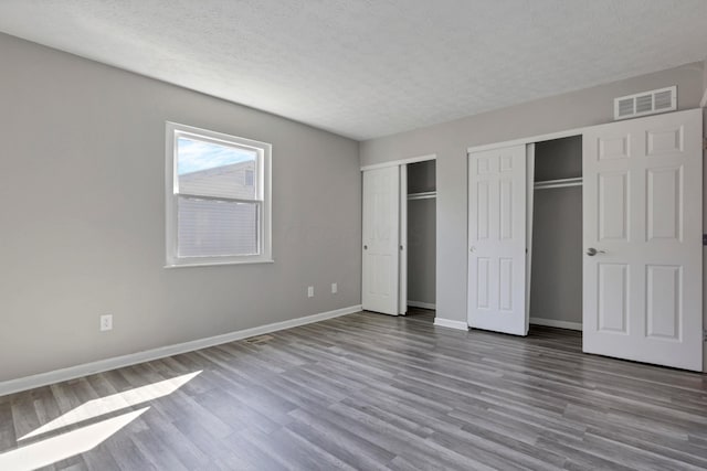 unfurnished bedroom featuring wood-type flooring, a textured ceiling, and two closets