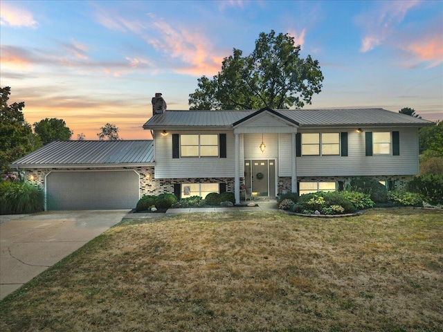 split foyer home featuring metal roof, a garage, driveway, a yard, and a chimney