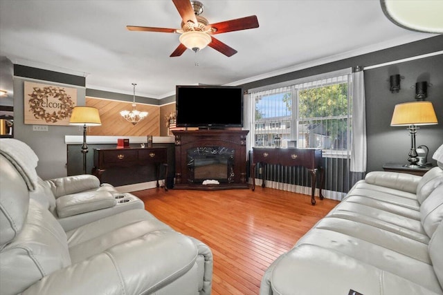 living room featuring wood-type flooring, ceiling fan with notable chandelier, crown molding, and a glass covered fireplace