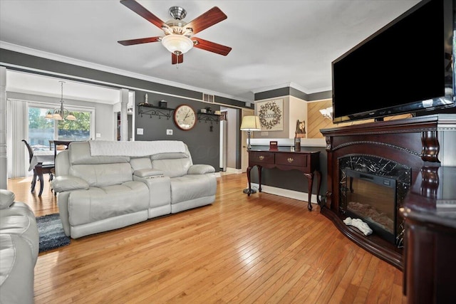 living area with ornamental molding, ceiling fan, hardwood / wood-style floors, and a glass covered fireplace