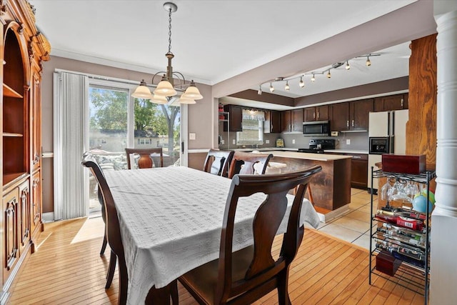 dining area featuring light hardwood / wood-style floors, an inviting chandelier, decorative columns, and crown molding