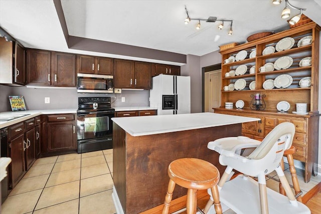 kitchen with a center island, white refrigerator with ice dispenser, black electric range, light tile patterned floors, and dark brown cabinetry