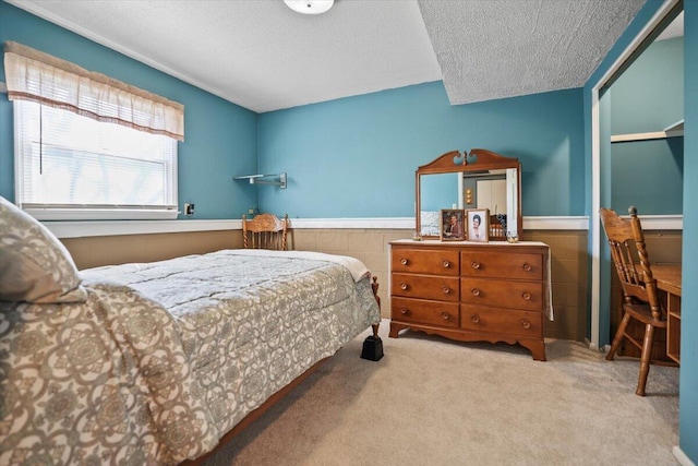 bedroom featuring a textured ceiling, carpet floors, and wainscoting