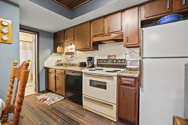 kitchen with under cabinet range hood, white appliances, a sink, light countertops, and dark wood finished floors