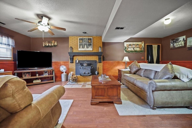 living room with hardwood / wood-style flooring, ceiling fan, a wood stove, and a textured ceiling