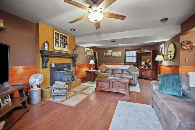 living room featuring hardwood / wood-style flooring, ceiling fan, a wood stove, and a textured ceiling