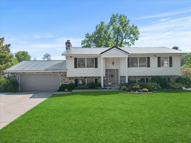 raised ranch featuring a chimney, metal roof, a garage, driveway, and a front lawn