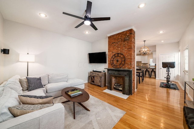 living room featuring ceiling fan with notable chandelier, wood-type flooring, and a fireplace