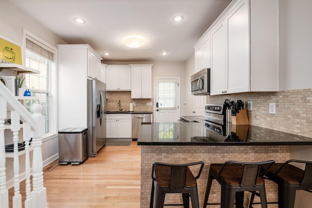 kitchen featuring kitchen peninsula, white cabinetry, stainless steel appliances, and light hardwood / wood-style flooring