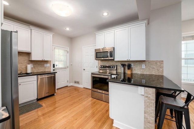 kitchen with a healthy amount of sunlight, white cabinetry, stainless steel appliances, and light wood-type flooring