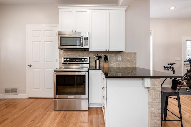 kitchen featuring a kitchen breakfast bar, white cabinetry, kitchen peninsula, and appliances with stainless steel finishes