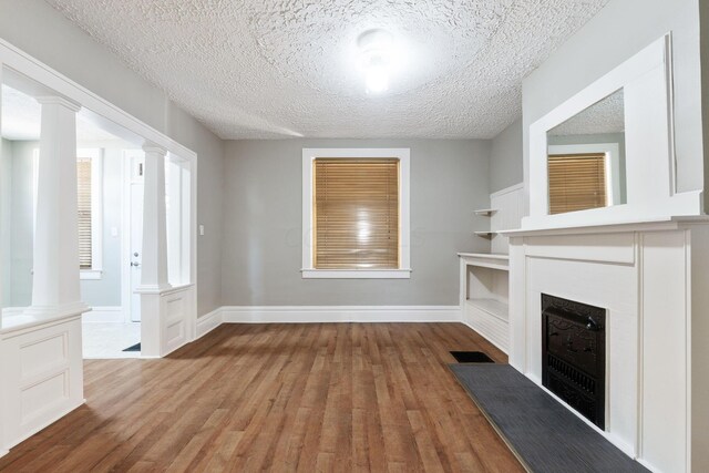 unfurnished living room with a textured ceiling, light hardwood / wood-style floors, and decorative columns