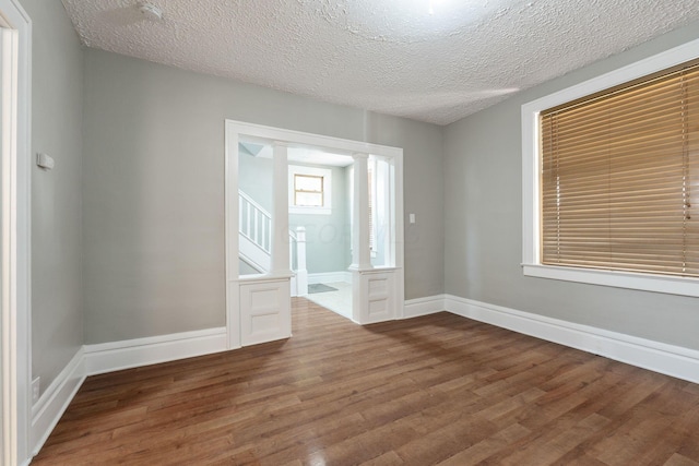 unfurnished room featuring decorative columns, dark wood-type flooring, and a textured ceiling