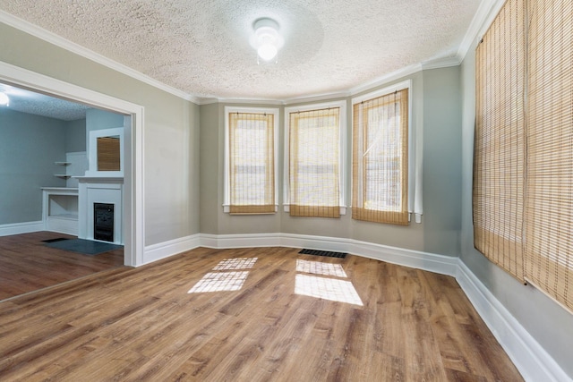 empty room with wood-type flooring, a textured ceiling, and ornamental molding