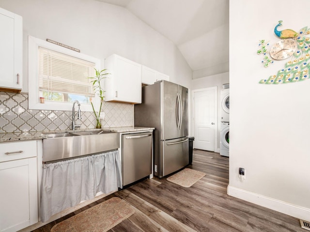 kitchen featuring dark hardwood / wood-style flooring, stainless steel appliances, white cabinets, stacked washer and dryer, and lofted ceiling