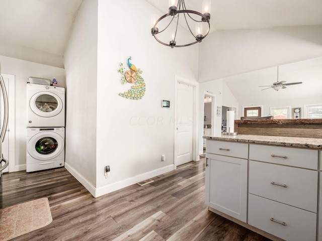 clothes washing area featuring ceiling fan with notable chandelier, dark hardwood / wood-style flooring, a towering ceiling, and stacked washer / dryer