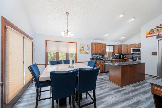 dining area with sink, an inviting chandelier, high vaulted ceiling, wood-type flooring, and a textured ceiling