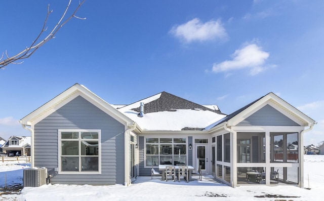 snow covered rear of property featuring a sunroom and central AC