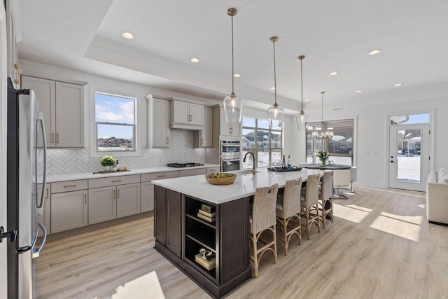 kitchen with stainless steel appliances, light wood finished floors, gray cabinetry, and tasteful backsplash