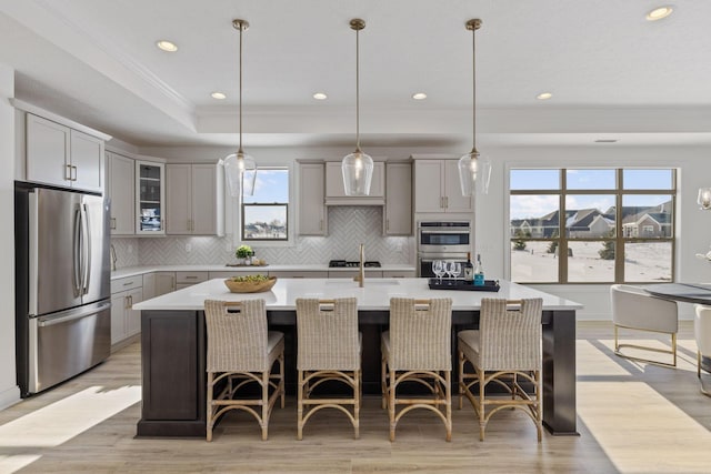 kitchen featuring gray cabinetry, light countertops, appliances with stainless steel finishes, decorative backsplash, and a raised ceiling