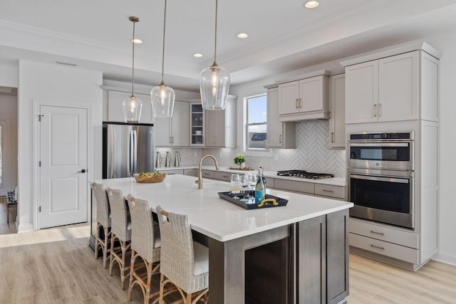 kitchen with a large island, light wood finished floors, light countertops, backsplash, and appliances with stainless steel finishes