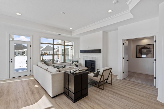 living area featuring light wood-type flooring, a raised ceiling, crown molding, and a glass covered fireplace