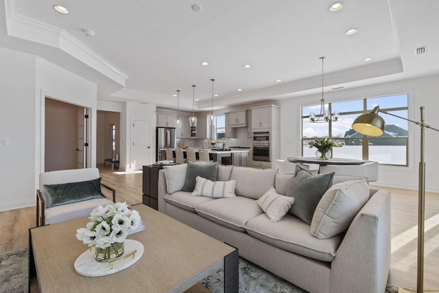 living area with a tray ceiling, crown molding, visible vents, light wood-style flooring, and a chandelier