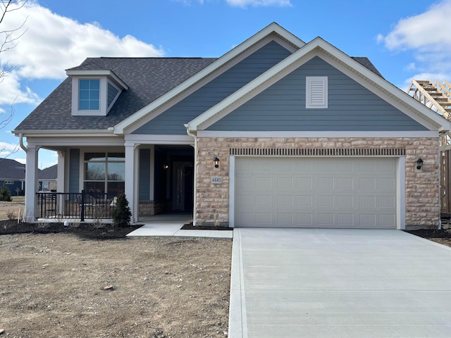 view of front of property featuring an attached garage, covered porch, a shingled roof, concrete driveway, and stone siding