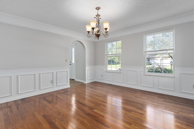 empty room featuring dark wood-type flooring, a chandelier, a textured ceiling, and ornamental molding